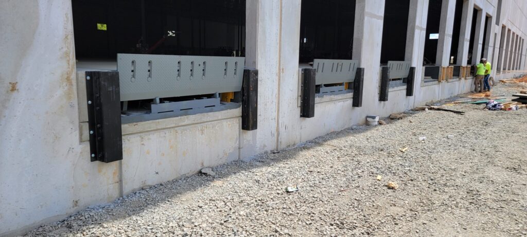 Loading dock bumpers and dock levelers installed on a concrete building; workers are visible in the background.