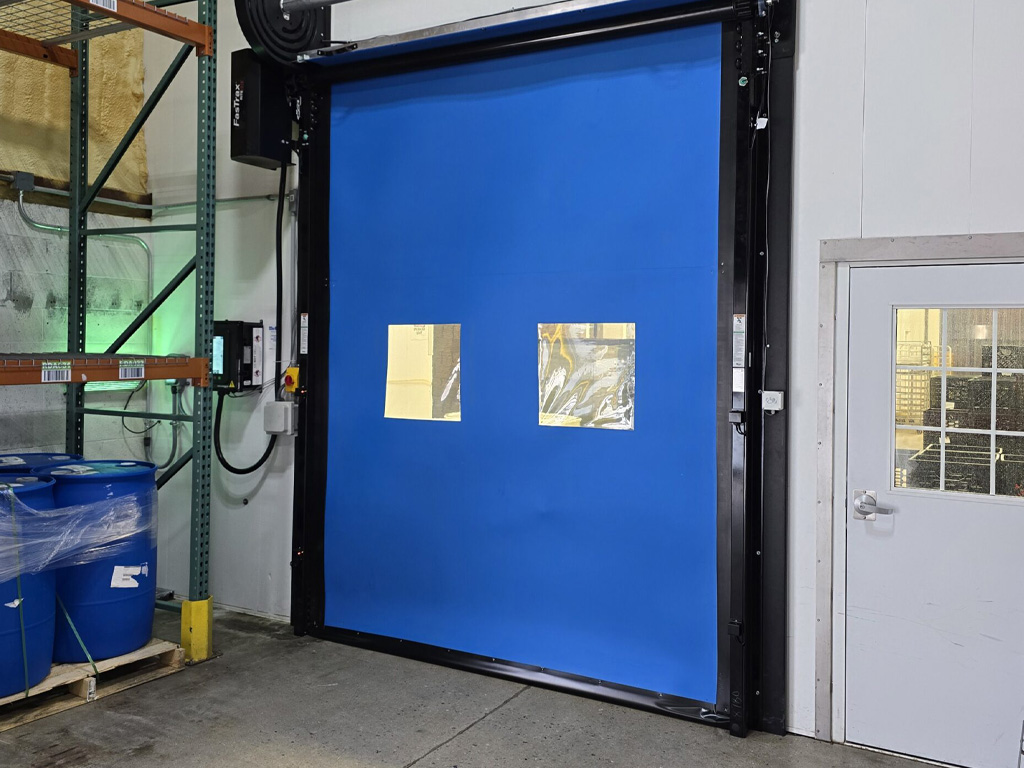 A blue industrial roll-up door with two clear windows next to a small white door inside a warehouse.