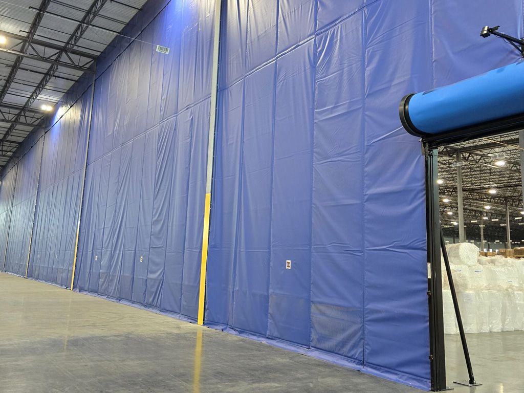 Large blue industrial curtains separate sections in a spacious warehouse with polished concrete floors.