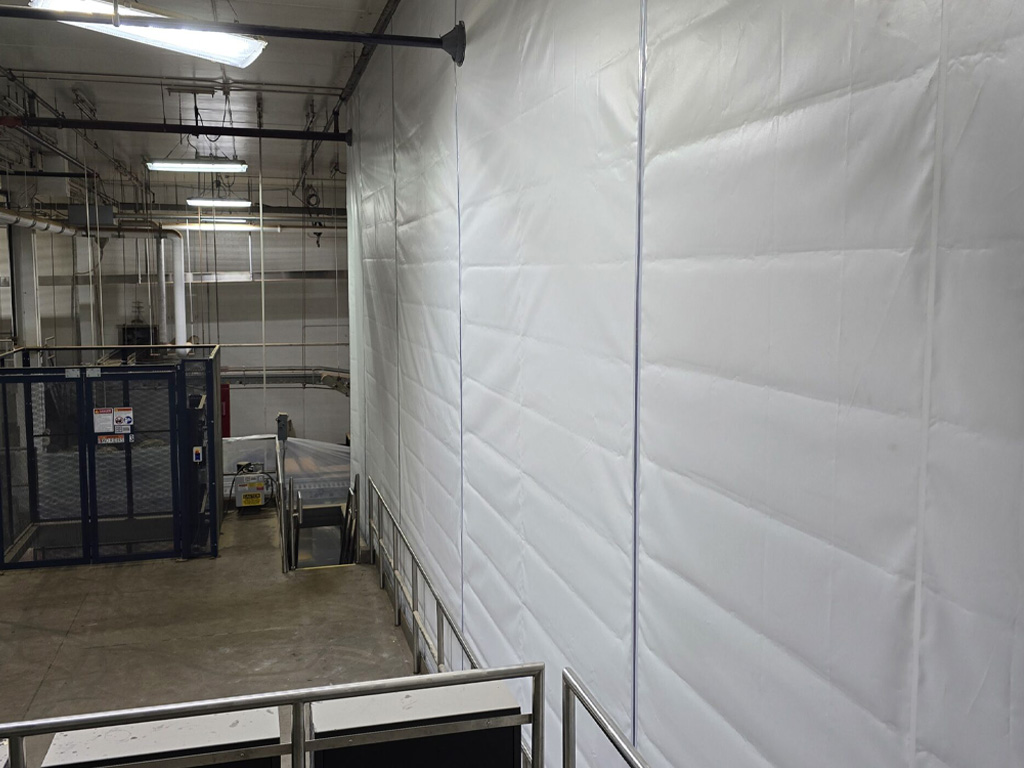 A factory interior with white insulated wall panels, metal railings, and industrial equipment in the background.