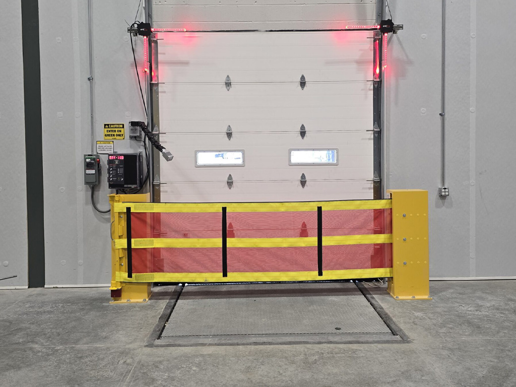 A yellow and red safety barrier blocks a closed loading dock door in a warehouse with concrete floors.