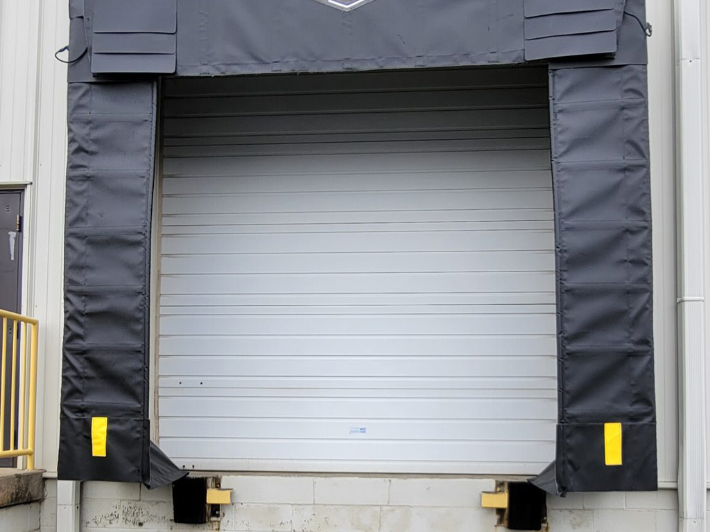 Closed industrial loading dock door with black padding on the sides and a yellow rail on the left.