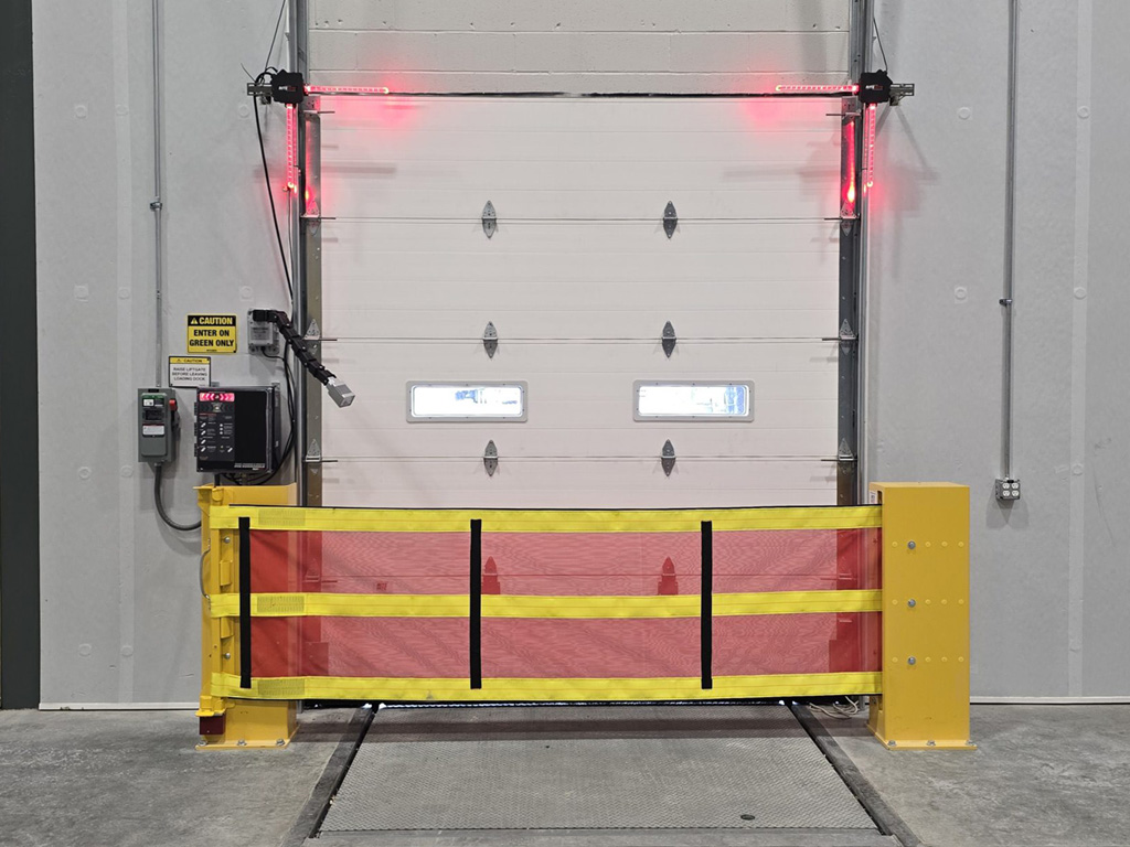 A loading dock door with a red and yellow safety barrier and red warning lights illuminated above.