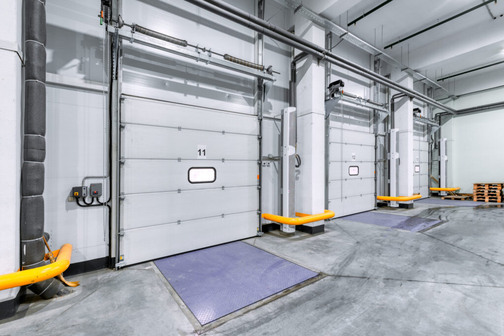 Three industrial loading dock doors with yellow bumpers and ramps in a clean, empty warehouse or distribution center.