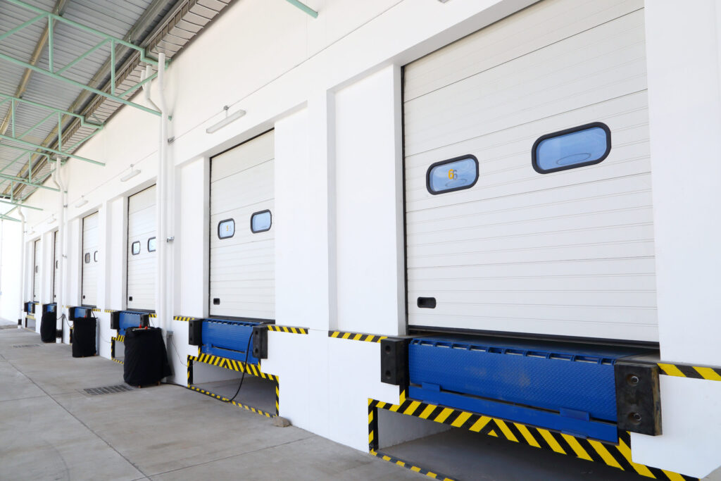 Five closed loading dock doors at a warehouse, with blue dock levelers and yellow-black safety markings.