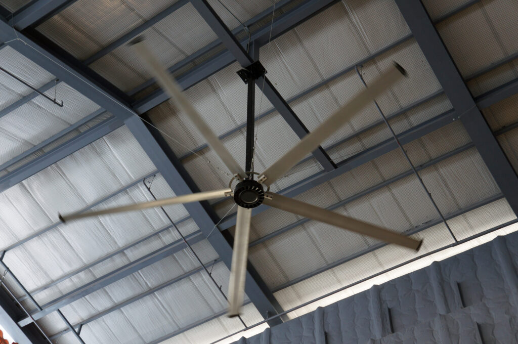 Large industrial ceiling fan with five blades spinning below a metal roof after expert industrial fan installation.