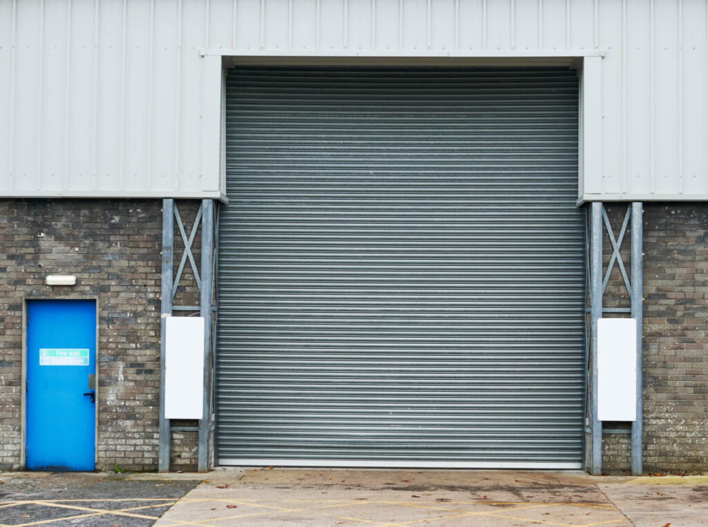 A large metal roller shutter door, high speed doors, with a blue side door on a brick industrial building.