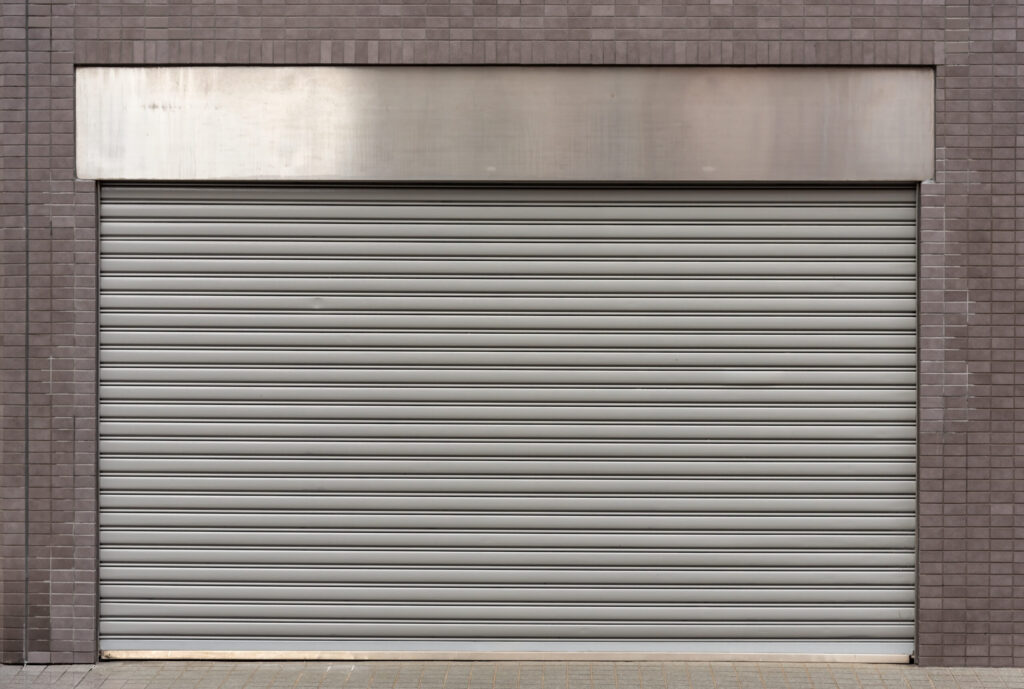 A closed gray rolling steel door set in a brick wall with a metallic fascia panel above it.
