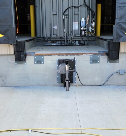 Warehouse loading dock with a raised metal dock leveler and a truck restraint system installed at the entrance.
