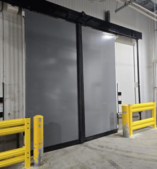Large gray industrial sliding door with yellow safety rails in a warehouse setting.