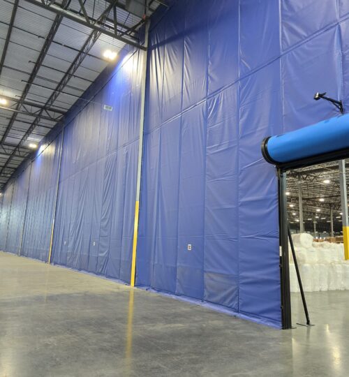 Large blue industrial curtain wall separates sections of a warehouse with visible lighting and polished concrete floor.